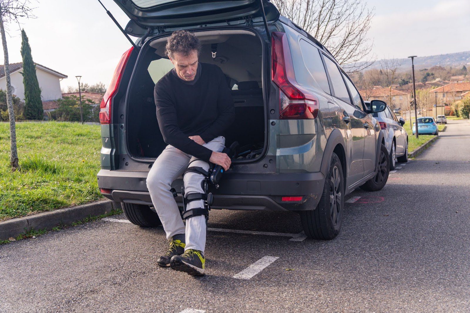 Patient sitting in the back of a van and adjusting a DREEVEN robotic knee brace. 
